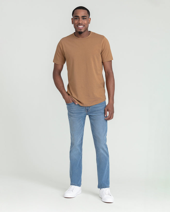 Man wearing tan short-sleeve t-shirt and light blue slim fit jeans with white sneakers.