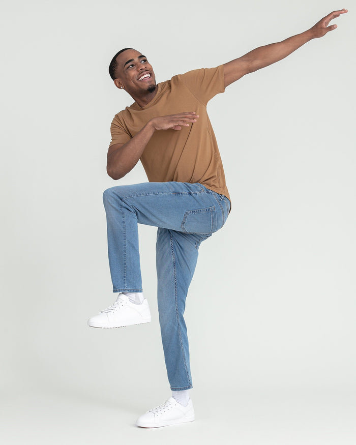 Man wearing light indigo slim fit jeans with tan t-shirt and white sneakers.