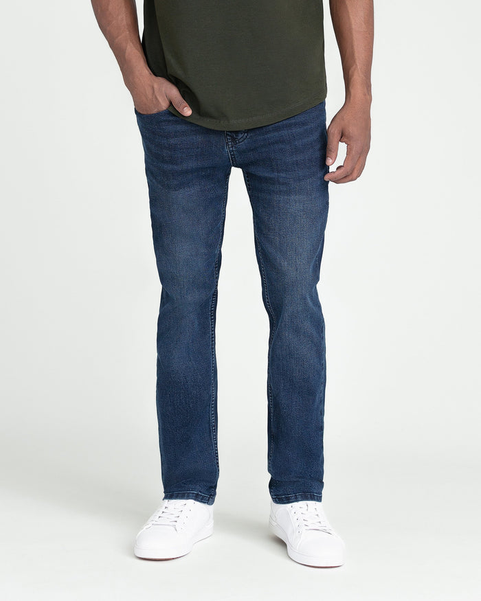 Man wearing dark blue slim fit jeans with olive green t-shirt and white sneakers.