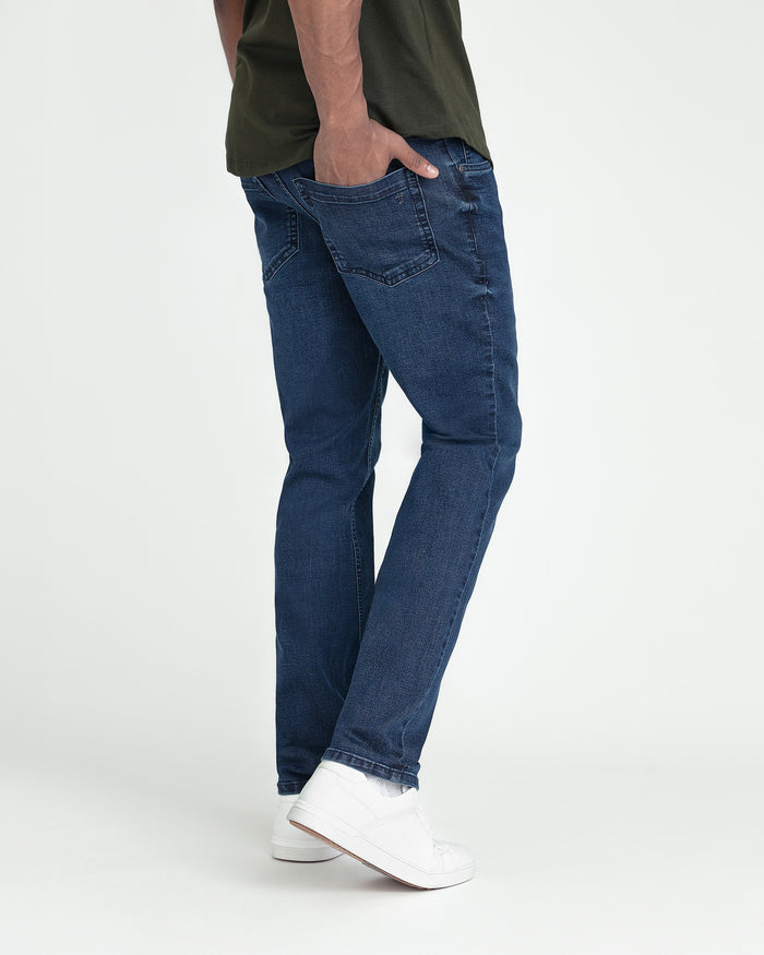 Man wearing dark blue slim fit jeans with white sneakers and olive shirt.