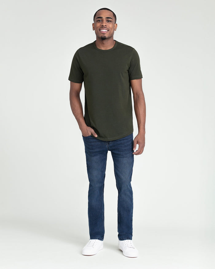 Man wearing olive green short-sleeve t-shirt, dark blue slim-fit jeans, and white sneakers.