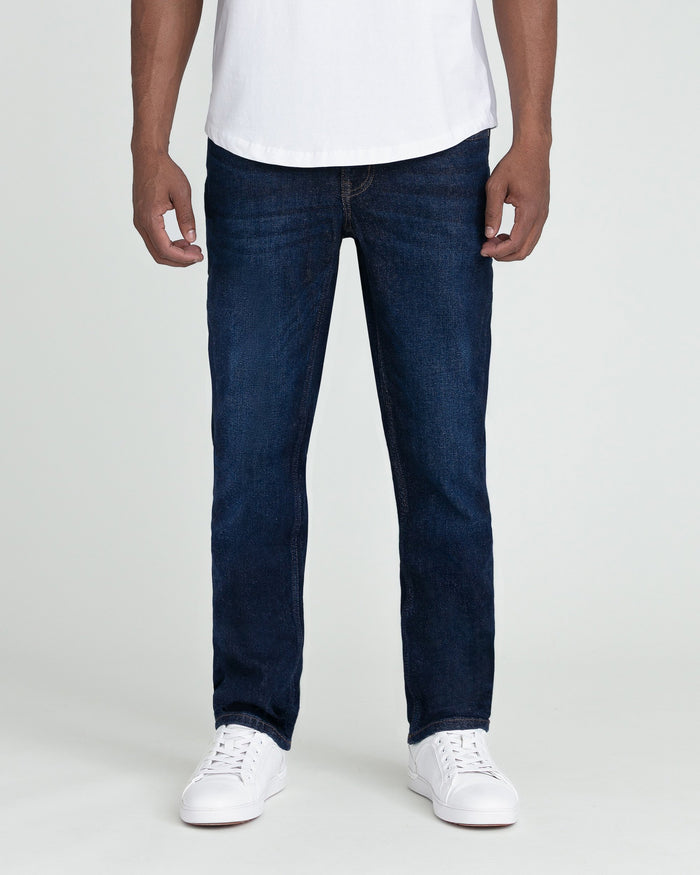 Man wearing white t-shirt and dark blue slim fit jeans with white sneakers.