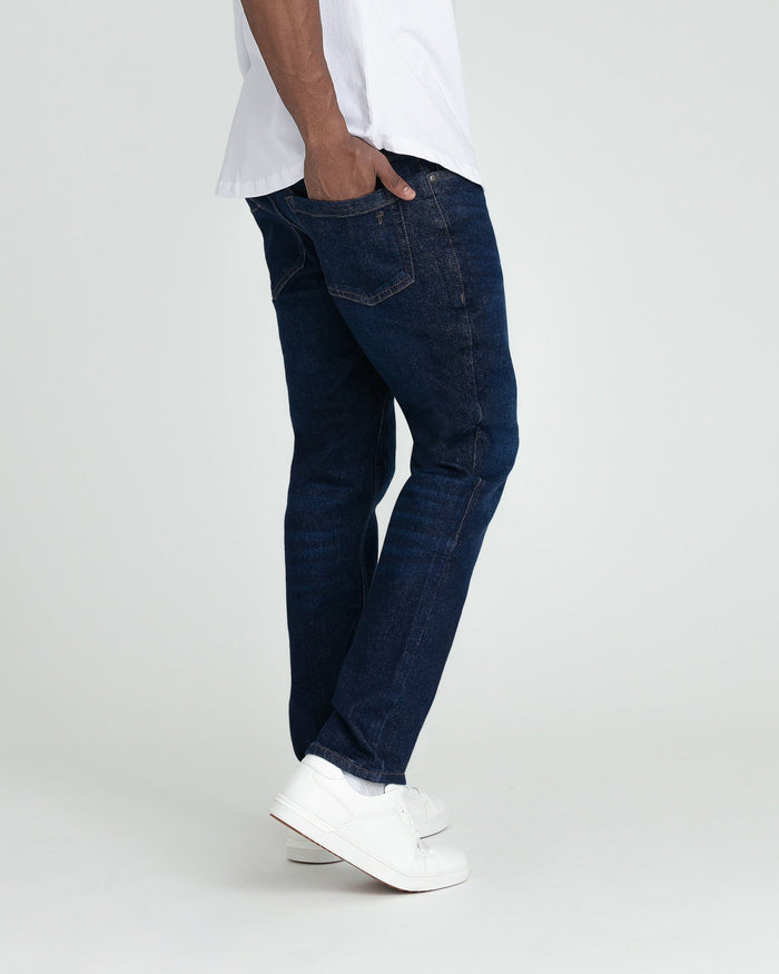 Man wearing dark blue slim fit jeans with white sneakers and white t-shirt.