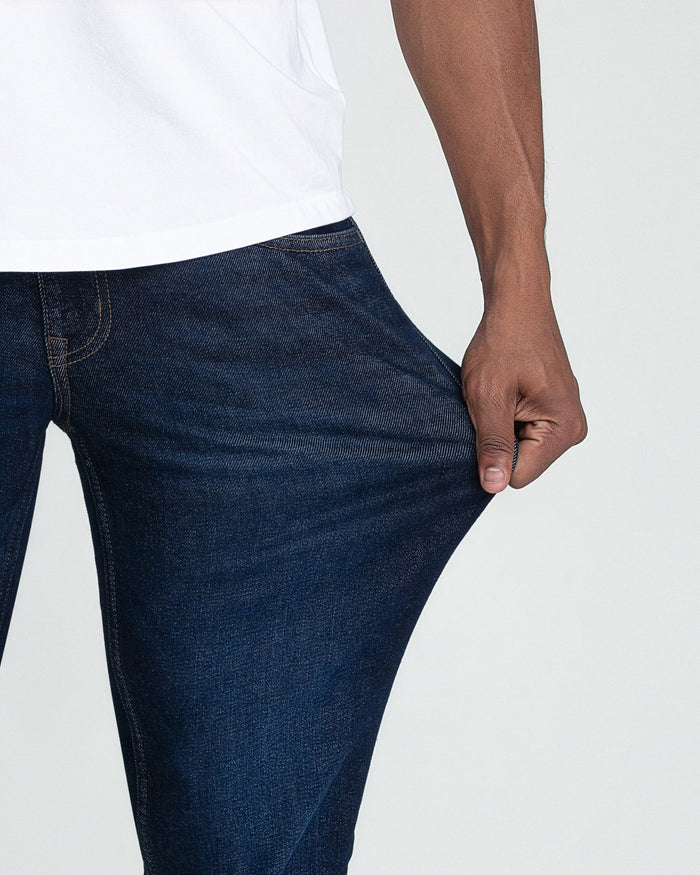 Dark blue slim fit jeans with visible stitching, worn with white shirt.