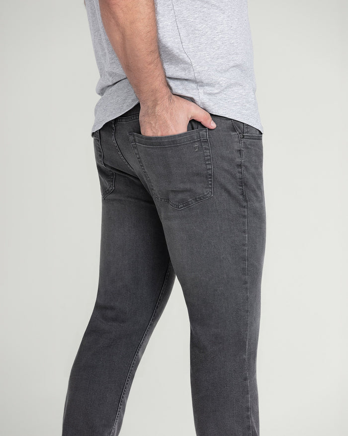 Man wearing light grey t-shirt and charcoal slim fit jeans with back pocket visible.
