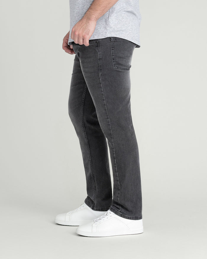 Man wearing grey t-shirt and charcoal slim fit jeans with white sneakers, side view.