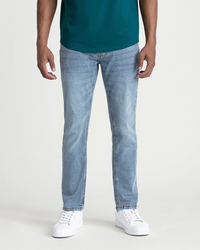 Man wearing teal t-shirt and light blue slim fit jeans with white sneakers.