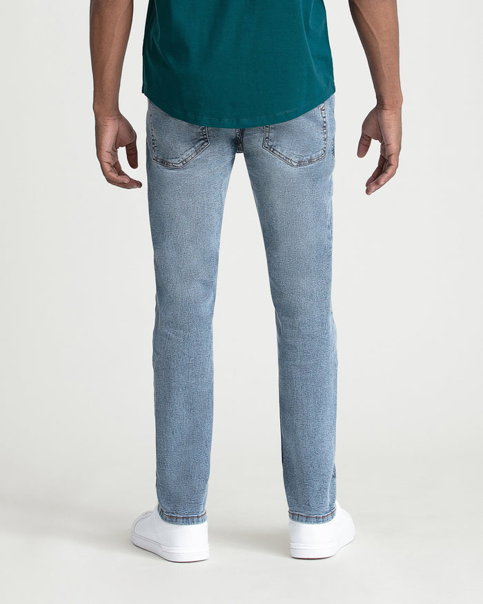 Man wearing light blue slim fit jeans and teal shirt, shown from waist down with white sneakers.