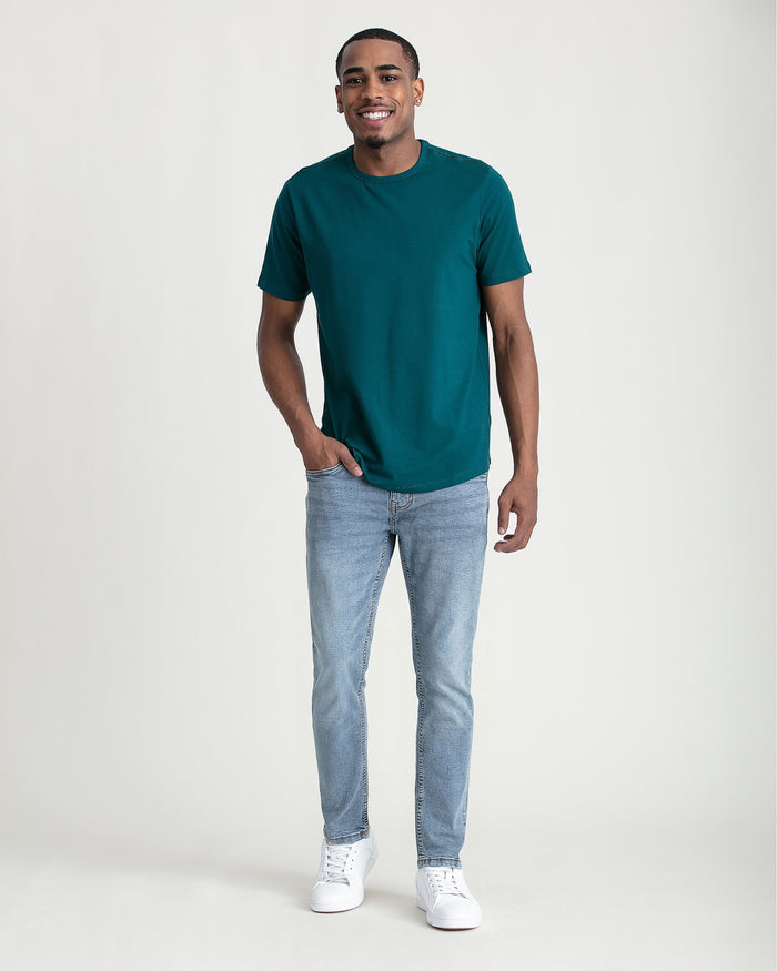 Man wearing teal short-sleeve t-shirt and light blue slim fit jeans with white sneakers.