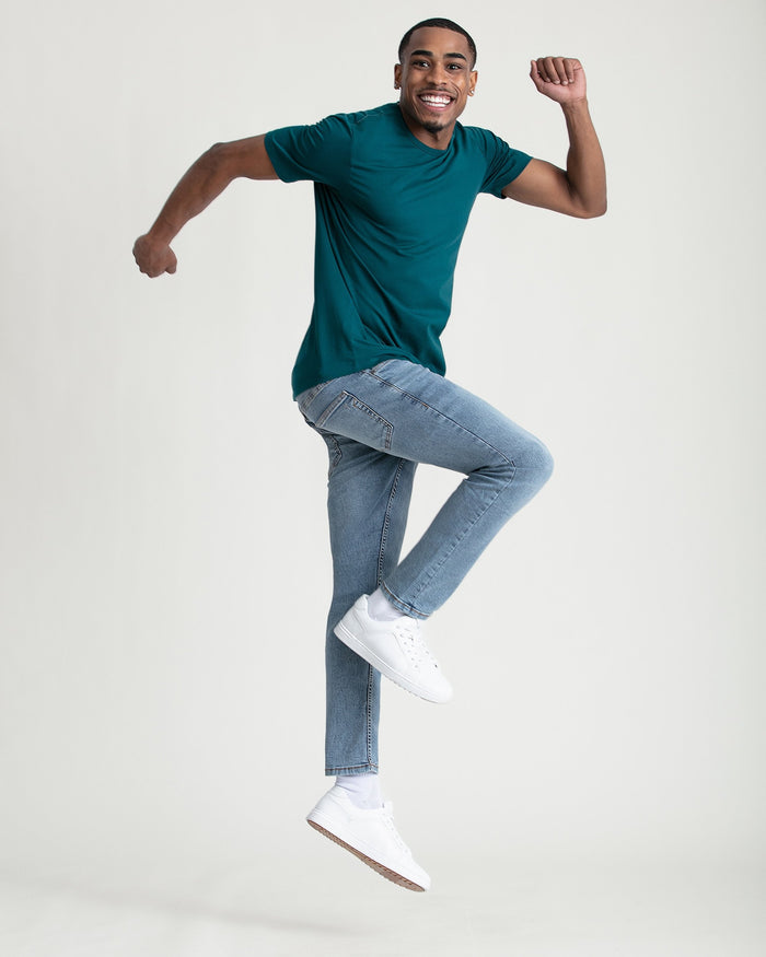 Man wearing teal short-sleeve t-shirt and light blue slim fit jeans with white sneakers.