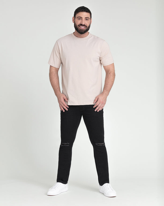 Man wearing cream short-sleeve t-shirt and black slim fit jeans with ripped knees, styled with white sneakers.
