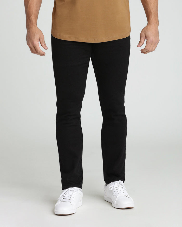 Man wearing tan t-shirt and black slim fit jeans with white sneakers.