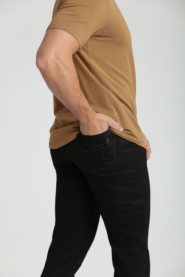 Man wearing tan short-sleeve t-shirt with black slim fit jeans, side view.
