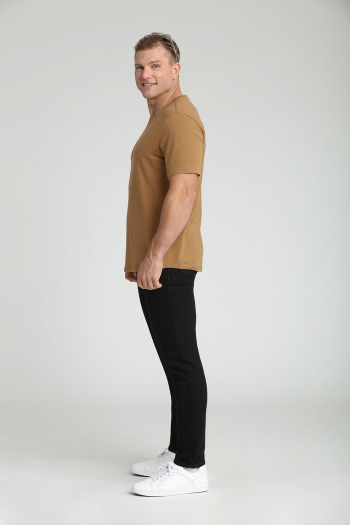 Man wearing tan short-sleeve t-shirt with black slim-fit jeans and white sneakers.