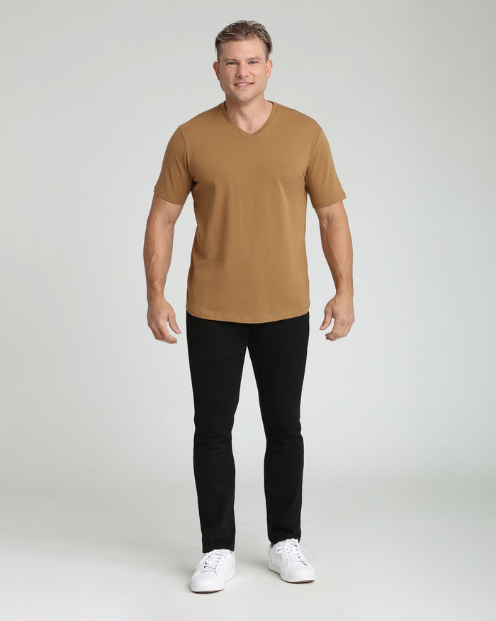 Man wearing tan V-neck short-sleeve shirt with black slim-fit pants and white sneakers.