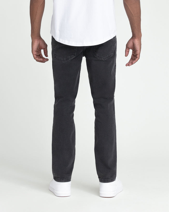 Man wearing white t-shirt and faded black slim fit jeans with white sneakers, shown from behind.