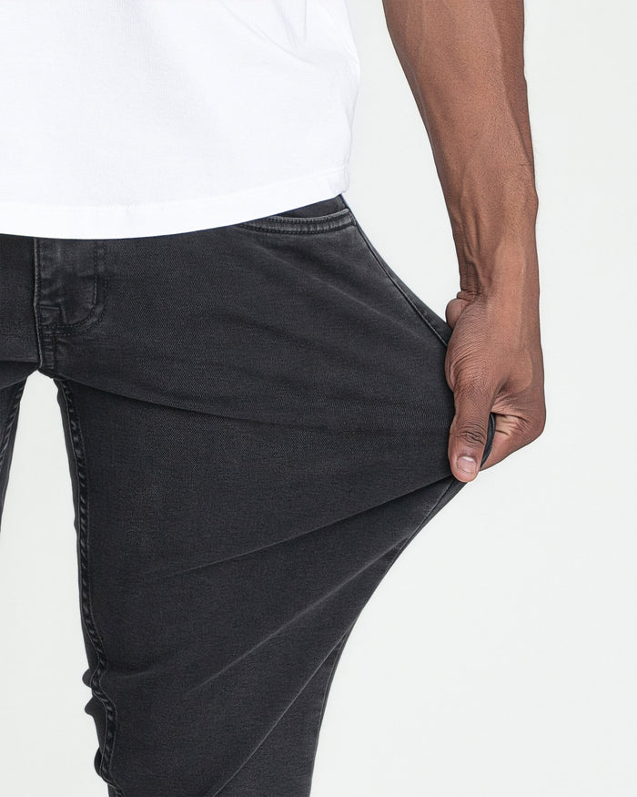 Faded black slim fit jeans with visible waistband and pocket detail on model wearing white shirt.