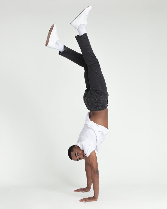 Person doing a handstand wearing faded black slim fit jeans, white shirt, and white sneakers.