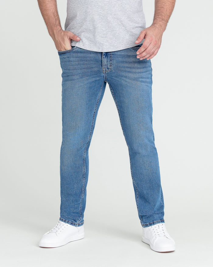 Man wearing medium blue slim fit jeans with gray t-shirt and white sneakers.