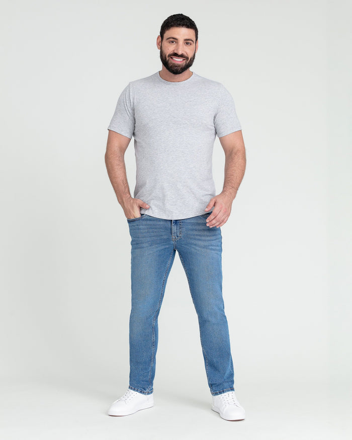 Man wearing light gray short-sleeve t-shirt and medium blue slim fit jeans with white sneakers.
