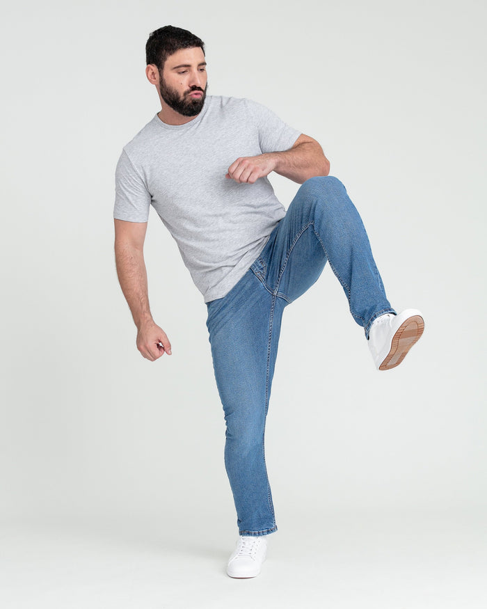 Man wearing gray t-shirt and medium blue slim fit jeans with white sneakers.