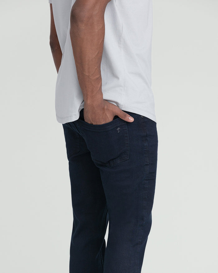 Man wearing white t-shirt and dark blue slim fit jeans with back pocket detail.