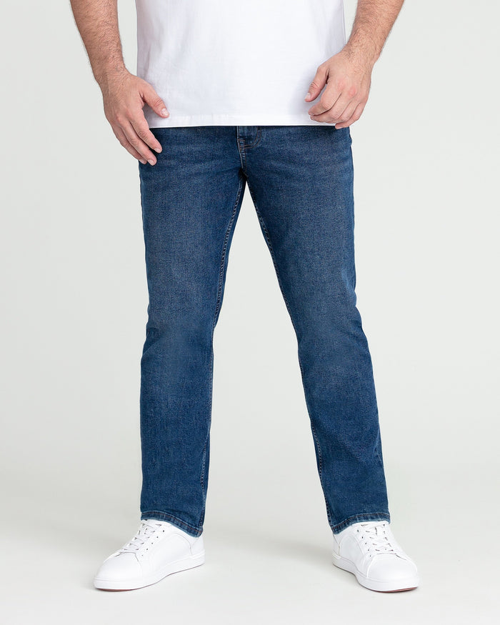 Man wearing medium blue slim fit jeans with white t-shirt and white sneakers.