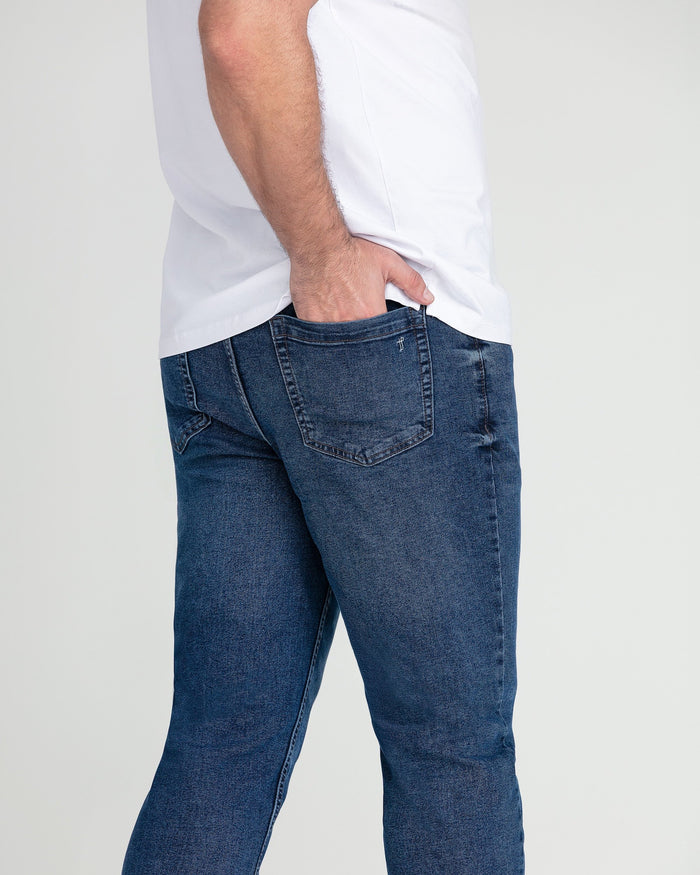Man wearing medium blue denim jeans with white t-shirt, shown from waist down in side profile.