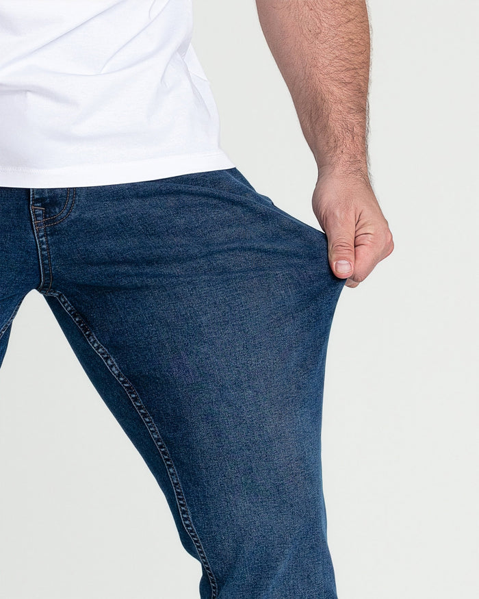 Man wearing medium blue slim fit jeans with white t-shirt, showing thigh and waistband detail.