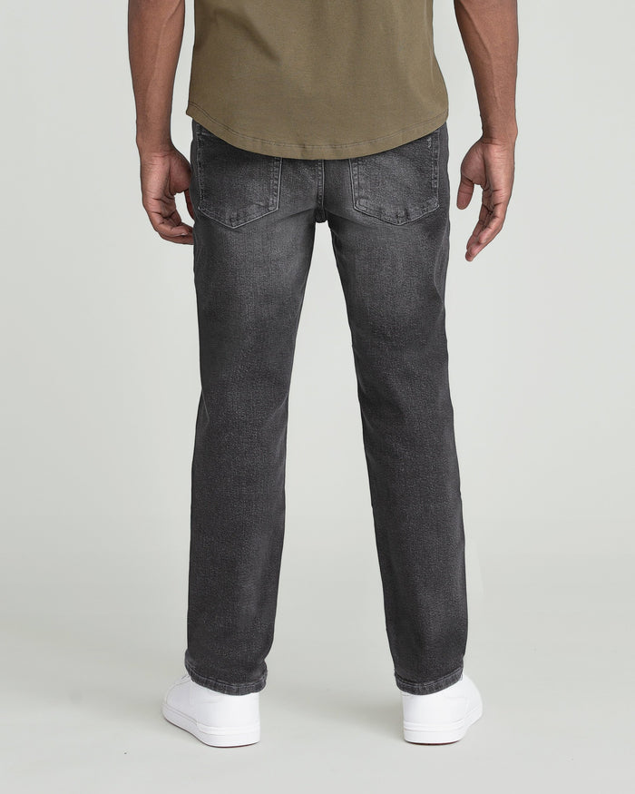 Man wearing grey jeans with five-pocket styling and tan t-shirt, shown from behind.