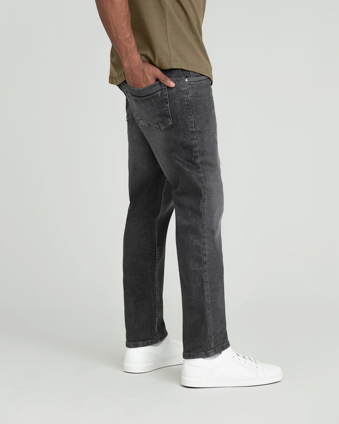 Man wearing gray Axel jeans with olive shirt and white sneakers, side view.
