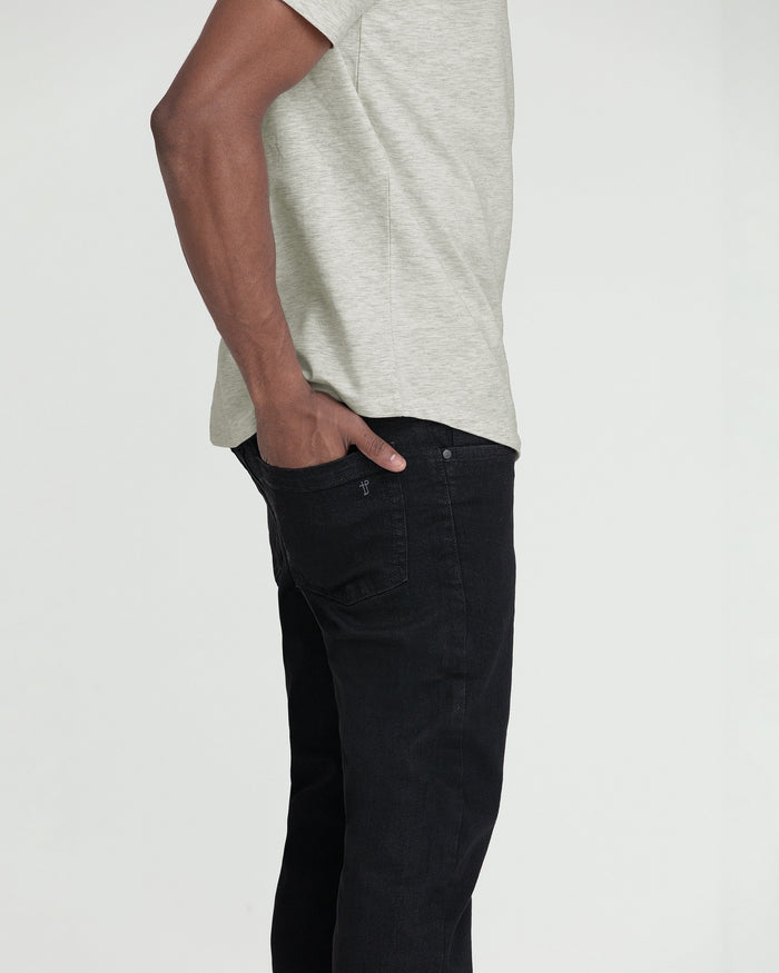 Man wearing light gray t-shirt and black slim-fit jeans with hand in pocket.