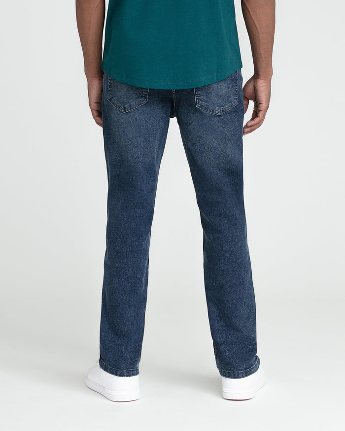 Man wearing teal t-shirt and dark blue jeans with white sneakers, back view.