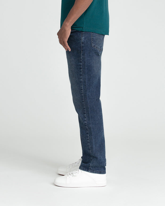 Man wearing dark indigo jeans and teal short-sleeve shirt with white sneakers, shown from side profile.