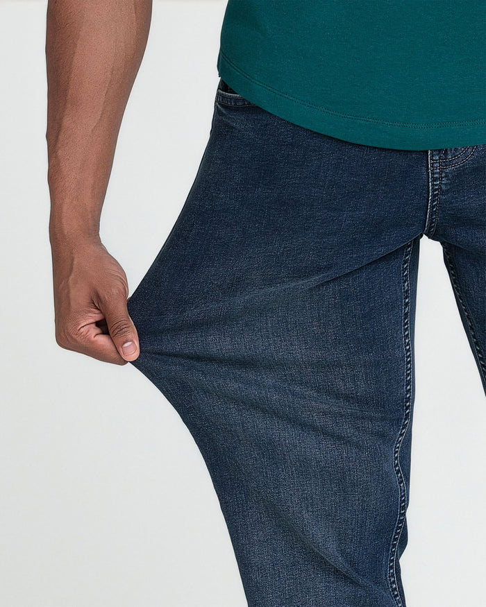 Man wearing midnight blue denim jeans with teal shirt, hand demonstrating fabric stretch.