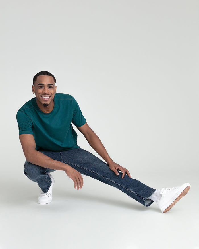 Man wearing dark teal short-sleeve t-shirt and dark denim jeans with white sneakers.