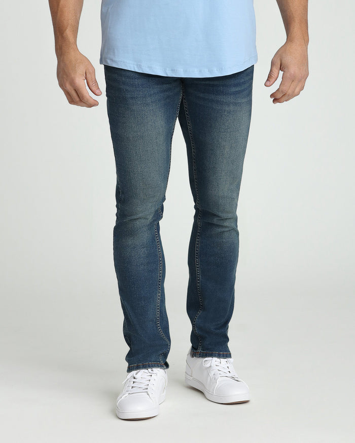 Man wearing light blue t-shirt and dark blue slim fit jeans with white sneakers.