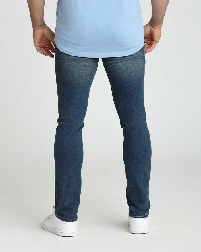 Man wearing light blue t-shirt and dark wash slim fit jeans with white sneakers, rear view.