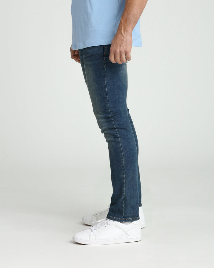 Man wearing light blue shirt and dark tinted slim fit jeans with white sneakers.