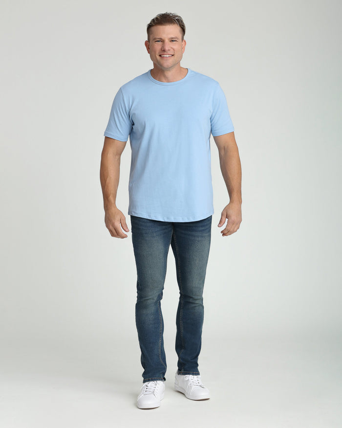 Man wearing light blue short-sleeve t-shirt and dark blue slim-fit jeans with white sneakers.