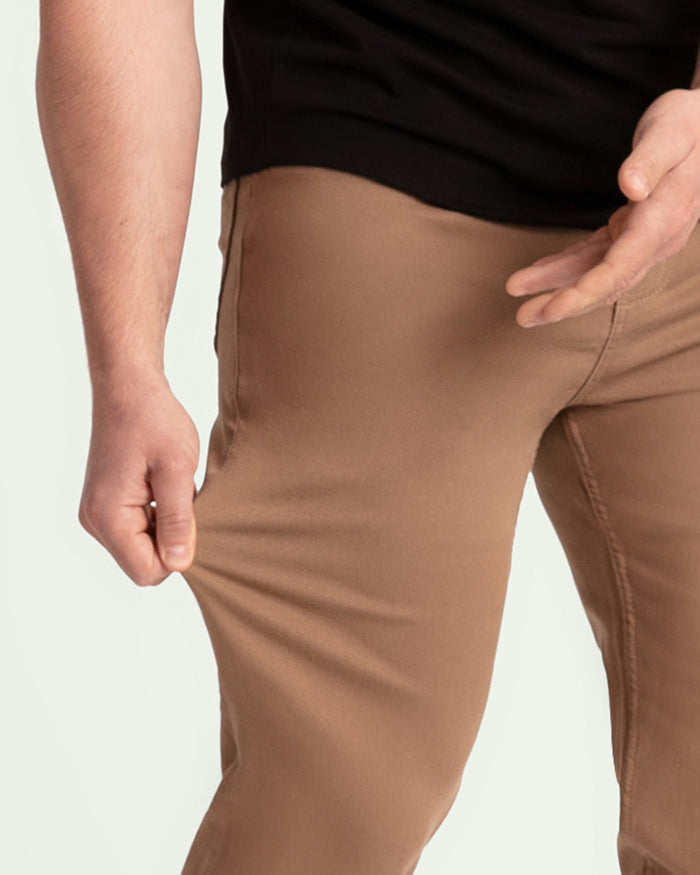 Man wearing dark khaki slim fit pants with black shirt, showing thigh and waist fit.