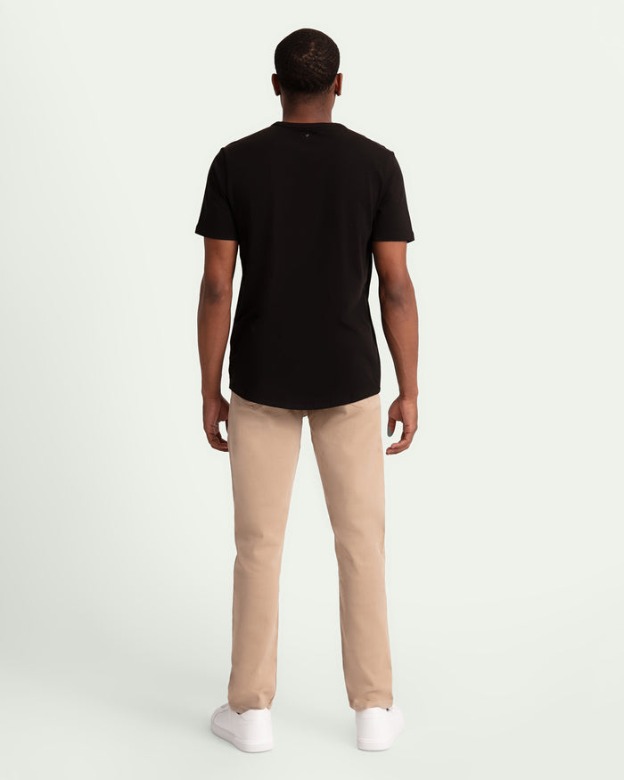 Man wearing black short-sleeve shirt and light khaki slim fit pants with white socks, shown from behind.