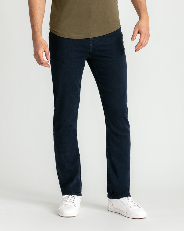 Man wearing olive-green t-shirt and dark navy slim fit jeans with white sneakers.