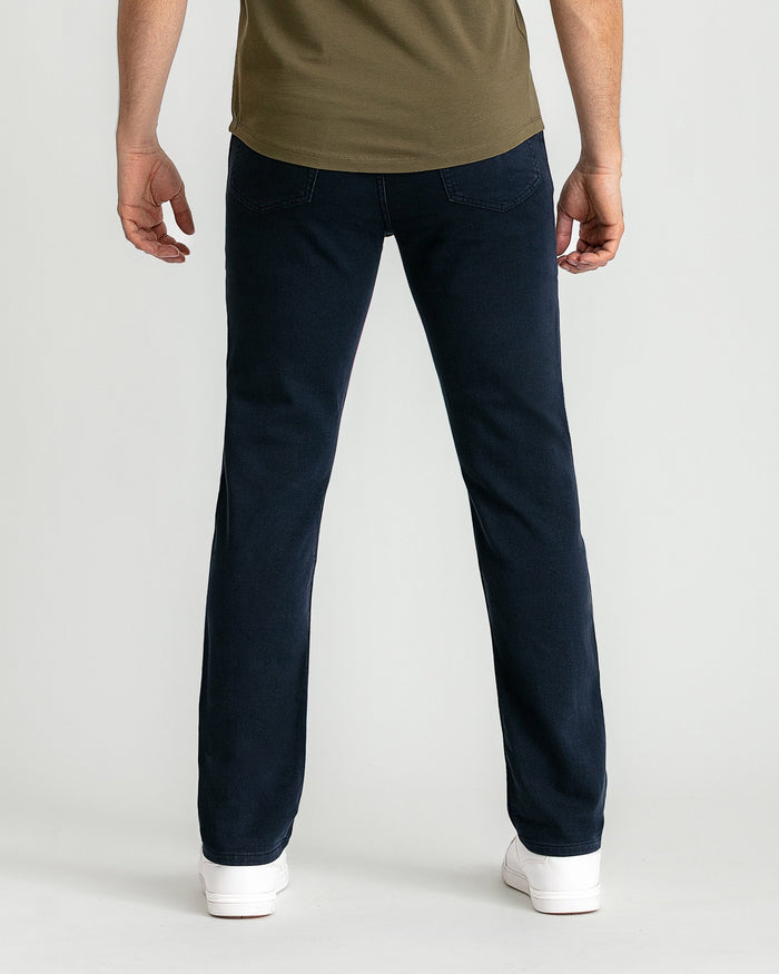 Man wearing olive-green t-shirt and dark navy slim-fit jeans with white sneakers.