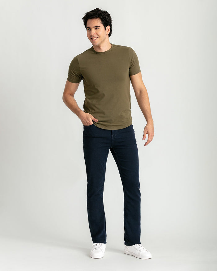 Man wearing olive-green short-sleeve crew neck t-shirt and navy slim fit jeans with white sneakers.