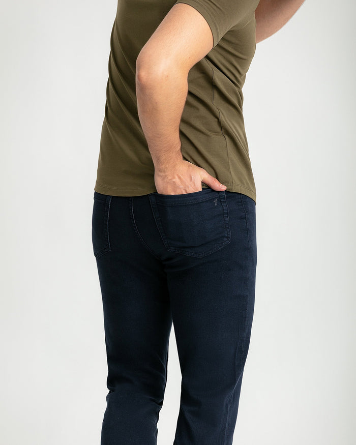 Man wearing olive t-shirt and navy slim fit jeans with hand in pocket.