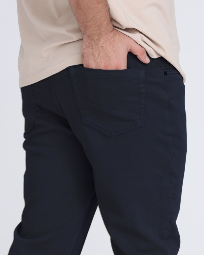 Man wearing navy slim fit pants with cream-colored shirt, close-up detail of waistband and pocket.