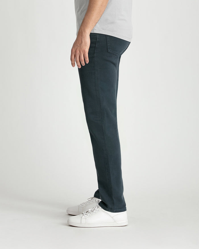 Man wearing slate-colored slim fit pants with white sneakers and light gray t-shirt, shown from side view.