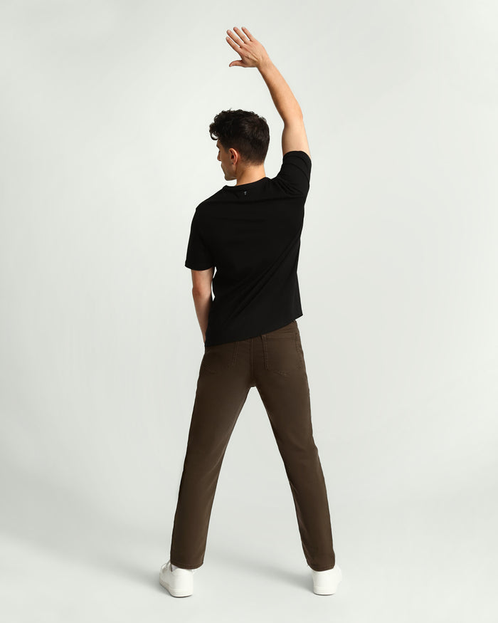 Man wearing black short-sleeve shirt and olive-colored slim fit pants, shown from behind with arm raised.