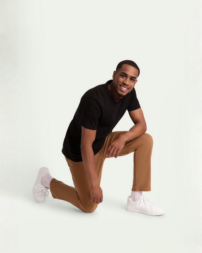 Man wearing black t-shirt and tobacco brown slim fit pants with white sneakers, kneeling pose.